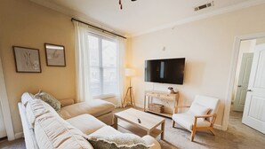 A living room with a sofa, coffee table, and armchair, a TV, and a lamp. - Belmont 2BR - Minutes to CaroMont | 14+ Nights (Belmont)