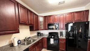 A kitchen with dark wooden cabinets, a granite countertop, a black stove, and a stainless steel refrigerator. - Belmont 2BR - Minutes to CaroMont | 14+ Nights (Belmont)