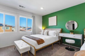 Une chambre à coucher comprenant un lit, un bureau, une chaise, une fenêtre avec vue et un mur d’accent de couleur verte.