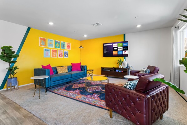 Un salon moderne avec un canapé bleu, un fauteuil en cuir rouge, une table basse et un téléviseur à écran plat fixé au mur, qui diffuse des services de streaming.