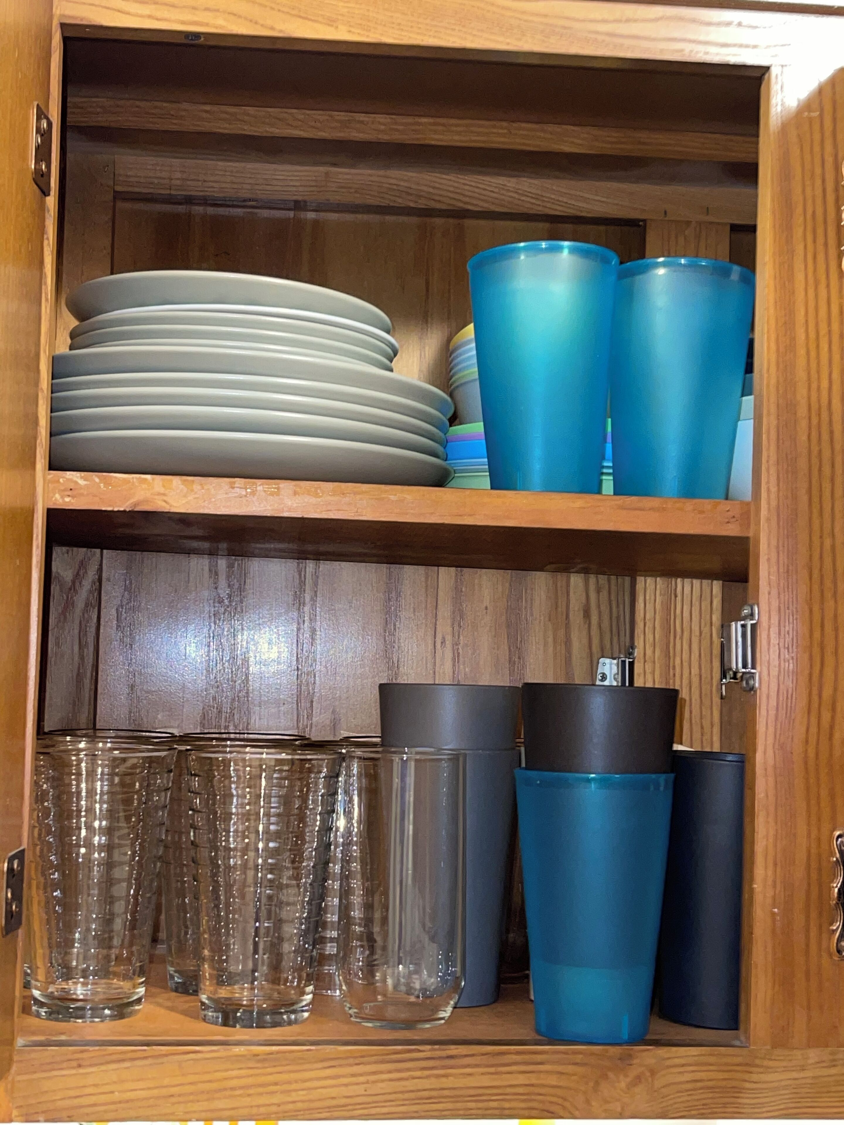 A wooden cabinet with shelves containing plates, cups, and glasses.
