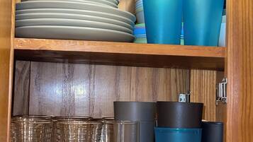 A wooden cabinet with shelves containing plates, cups, and glasses.