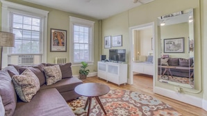 A living room with a sofa, a small table, a TV, and a mirror. - Sunny, 2 Bedroom Apt near Johns Hopkins, Charles Village - Explore Baltimore! (Maryland)