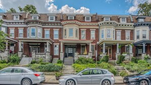 A row of three-story townhouses with a central entrance and steps leading up to the front door. - Sunny, 2 Bedroom Apt near Johns Hopkins, Charles Village - Explore Baltimore! (Maryland)