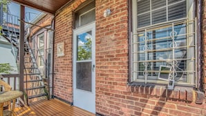 A brick building with a wooden deck, a white door, and a window with metal bars. - Sunny, 2 Bedroom Apt near Johns Hopkins, Charles Village - Explore Baltimore! (Maryland)