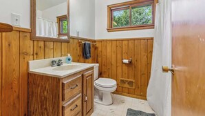 A bathroom with wooden walls, a white sink, a toilet, and a window with a view of greenery.