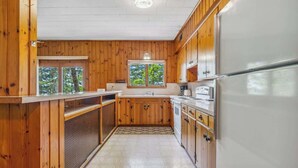 A kitchen with wooden cabinets, a white refrigerator, and a window with a view of trees.