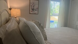 Un lit bien fait, avec du linge de lit blanc et plusieurs oreillers, une lampe fixée au mur et un tableau représentant un cheval.