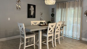 Un coin repas avec une table en bois et des chaises blanches, un lustre et un tableau représentant un cheval accroché au mur.