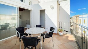 Ein Balkon mit rundem Tisch, vier Stühlen, einem Blumentopf und Blick auf die Straße.