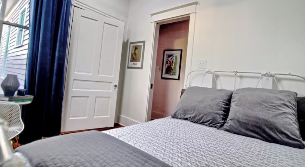Un dormitorio con cama, mesita de noche, silla y puerta.