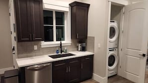 A kitchen with dark cabinets, a white countertop, a stainless steel dishwasher, and a built-in washer and dryer.