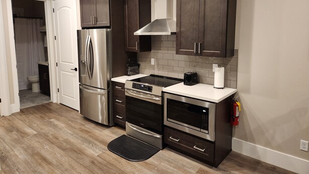 A modern kitchen with dark cabinets, stainless steel appliances, and a tiled backsplash.