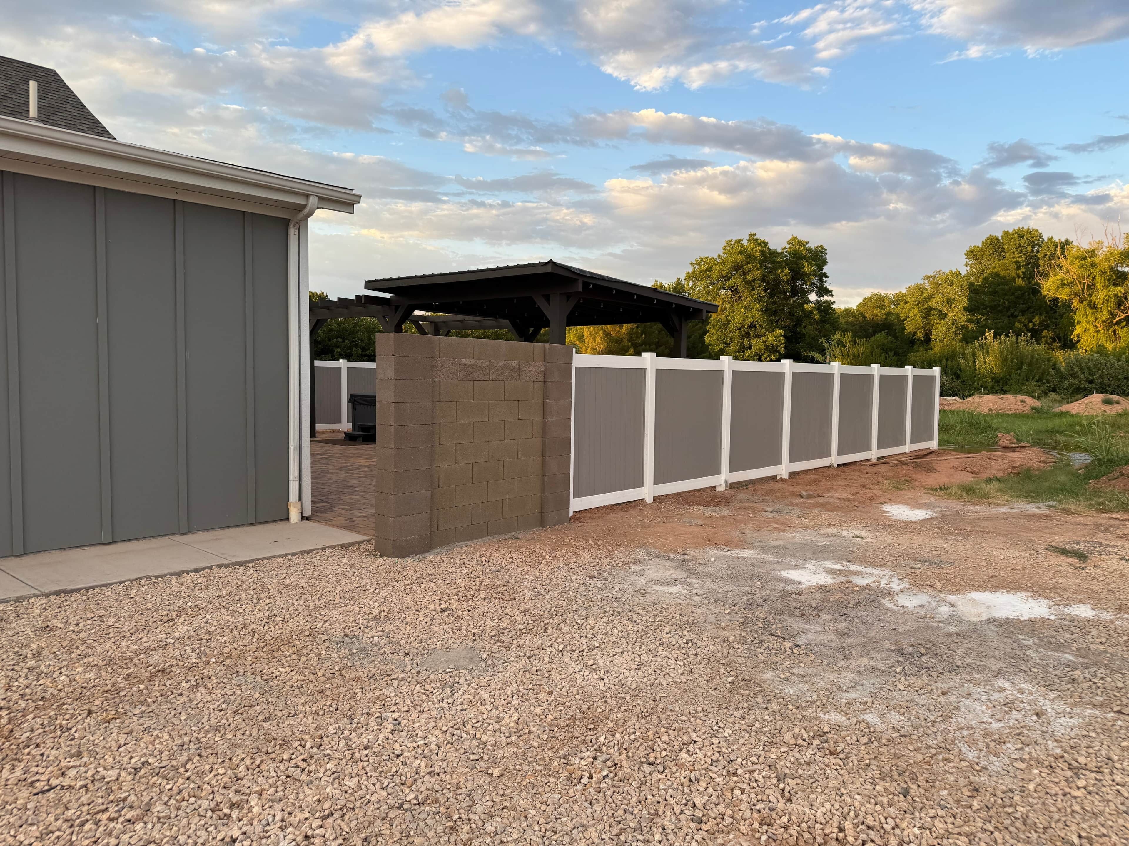 A gravel driveway leading to a fenced area with a covered structure and a shed.
