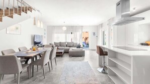 Un salon moderne comprenant un coin repas, un canapé et une cuisine équipée d’une hotte en acier inoxydable.