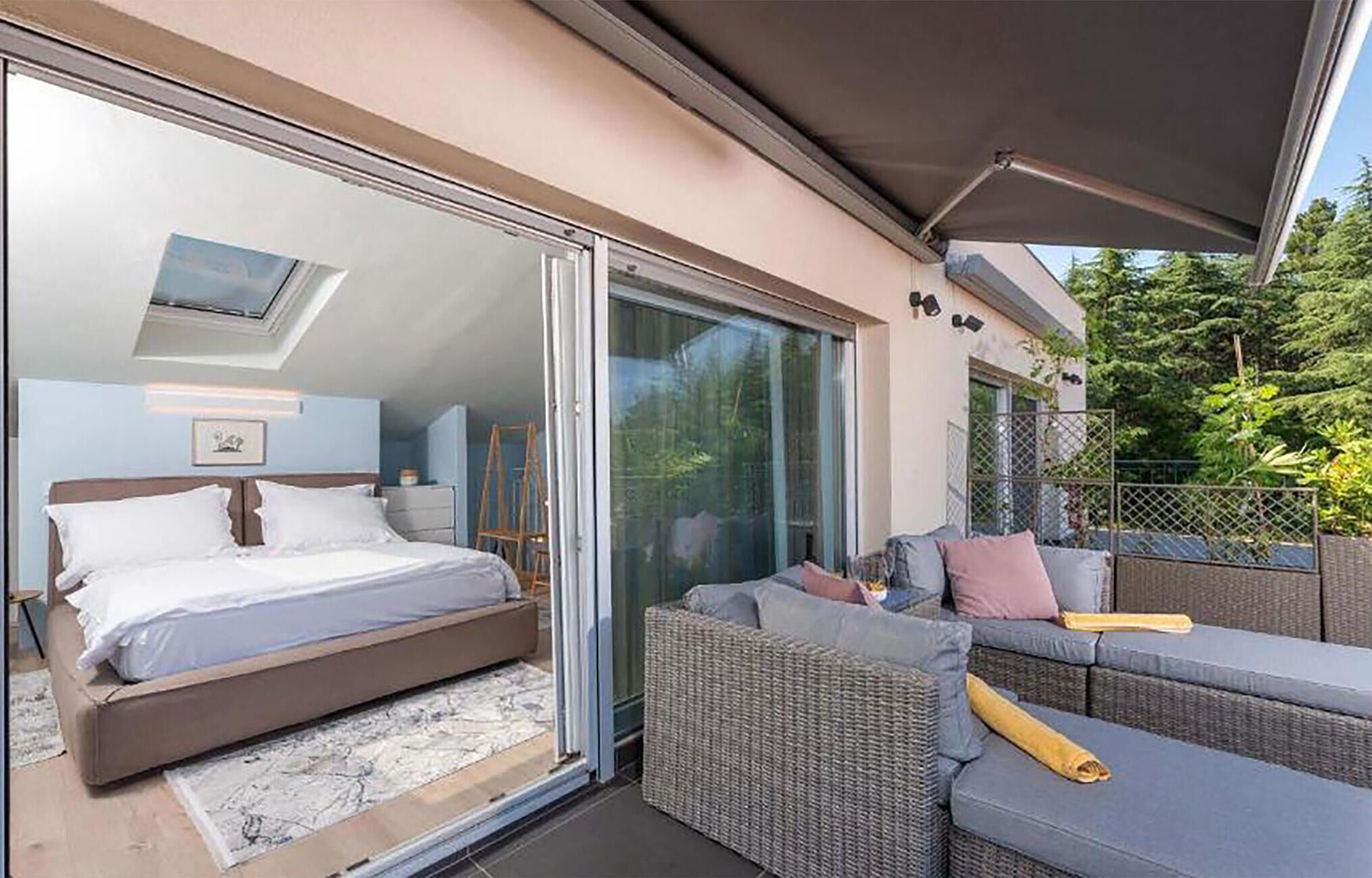 Et soveværelse med seng, balkon med fletmøbler og en stor skydedør af glas.