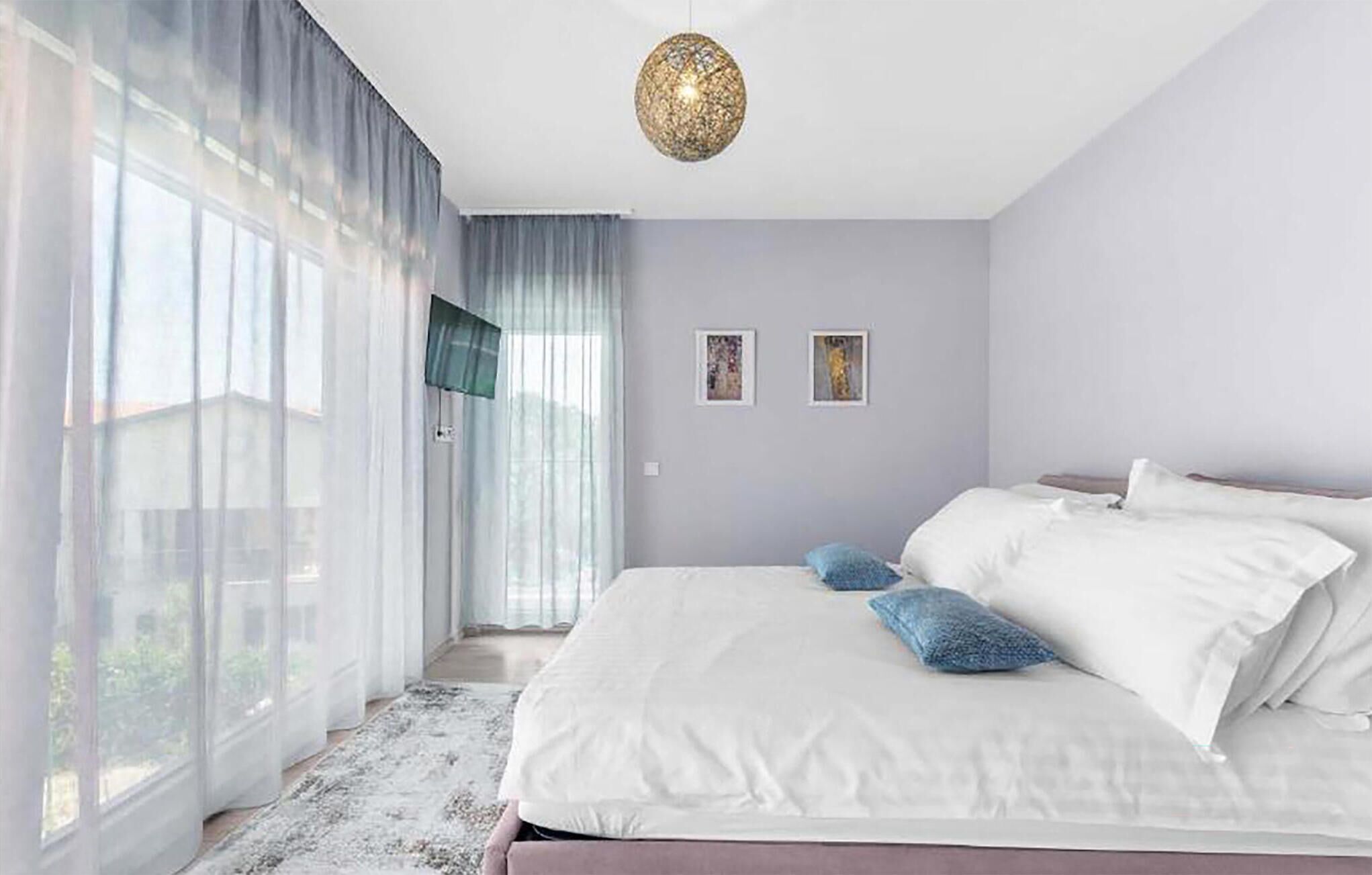 Ein Schlafzimmer mit einem großen Bett, Blick durch leichte Vorhänge und einer Pendelleuchte.