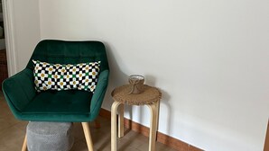 A room with a green armchair, a small stool, and a woven stool with a cushion.