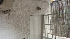 A small room with a white door, a table with two chairs, a window with a bamboo screen, and an air conditioning unit.