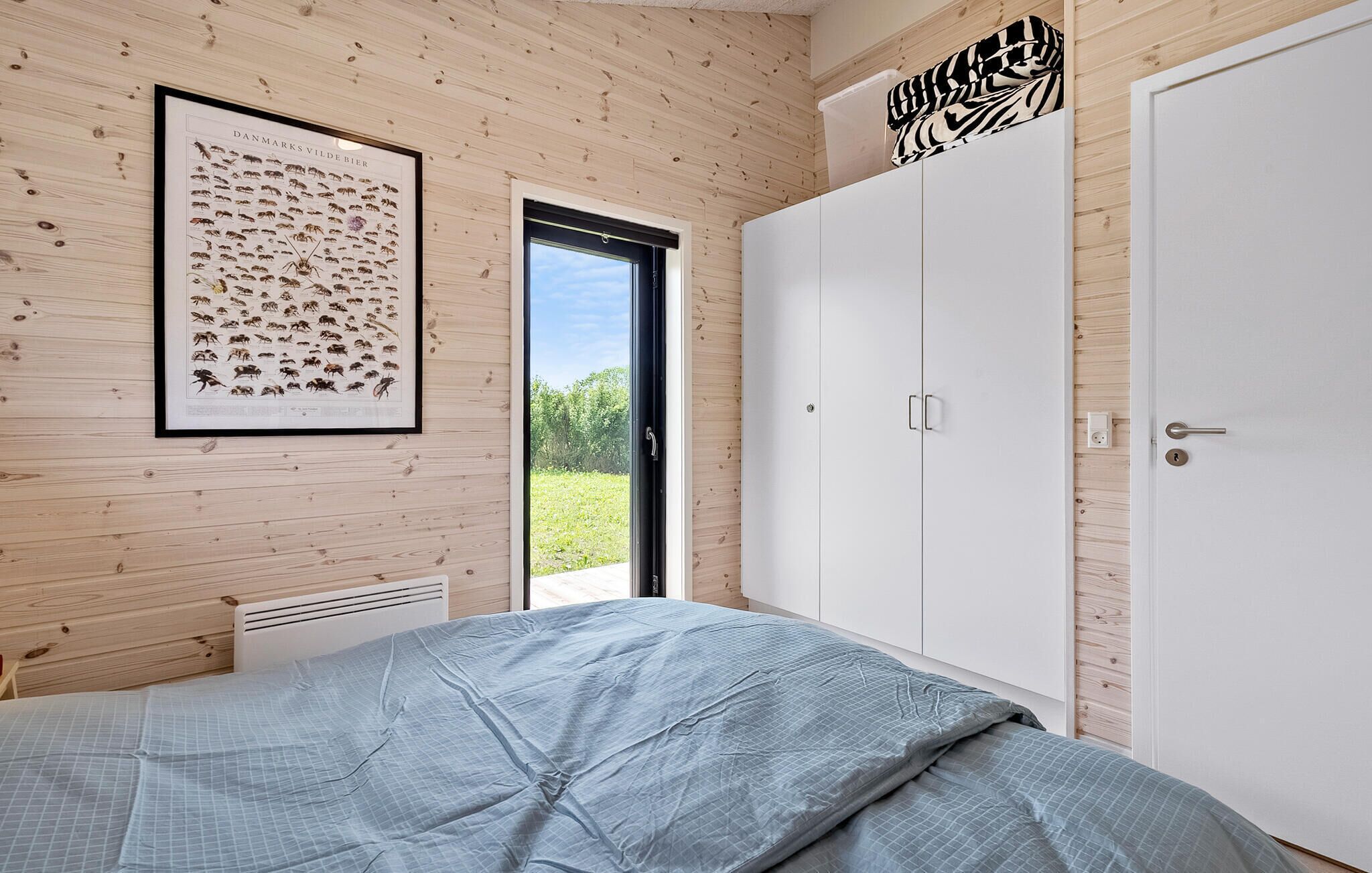 Un dormitorio con cama, armario, un cuadro con ilustraciones de insectos y una puerta que da a un jardín.