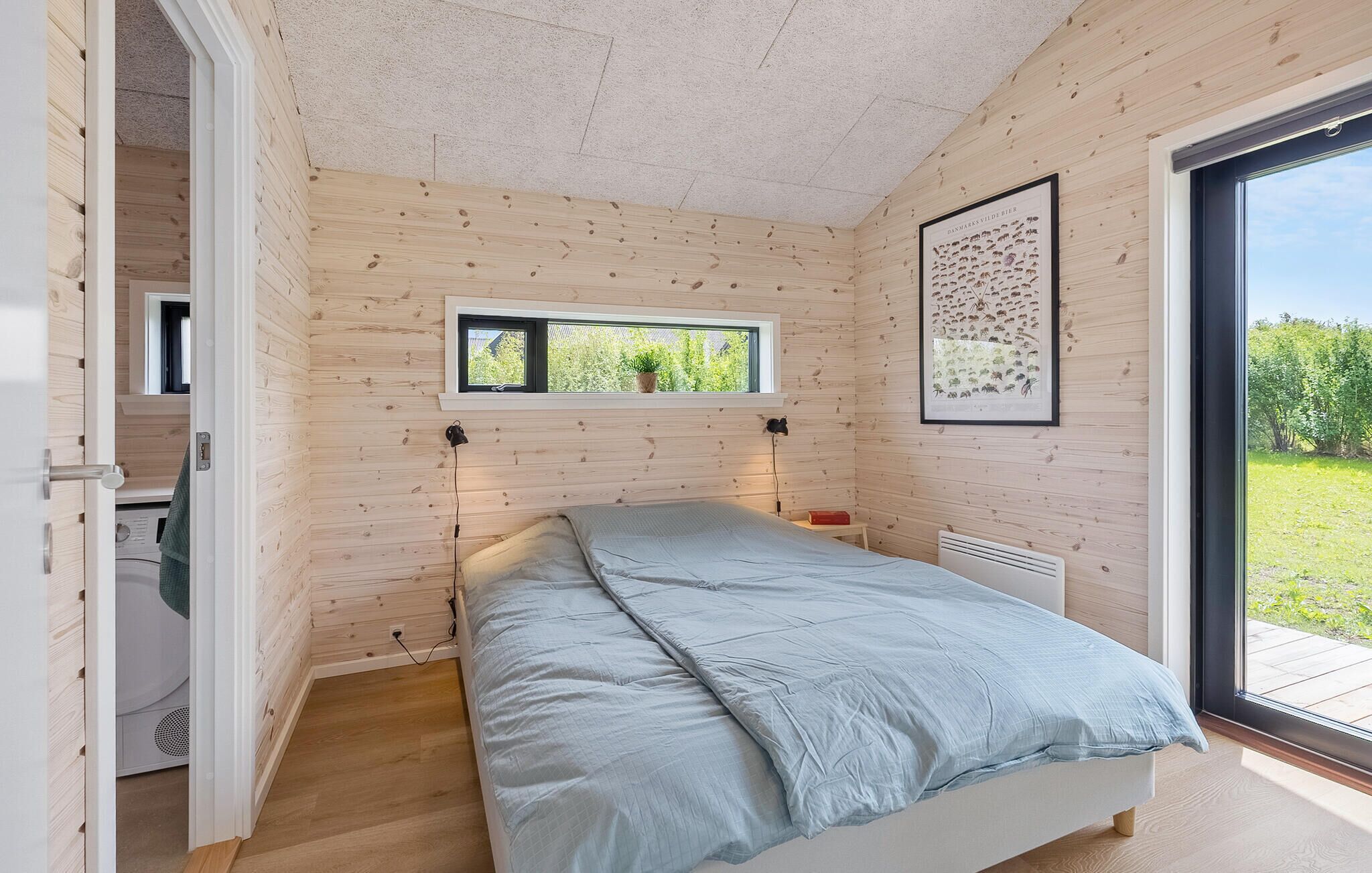 Un dormitorio con cama, ventana, radiador y puerta que da a otra habitación.