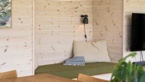 Um quarto acolhedor com paredes de madeira, uma cama com um cobertor verde, um travesseiro xadrez, uma luminária pequena e uma televisão na parede.