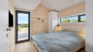 Quarto com cama, janela, porta e uma pequena mesa de cabeceira.