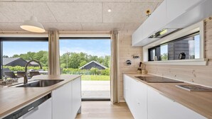 Cozinha moderna com uma ilha grande, armários brancos e vista para o exterior.