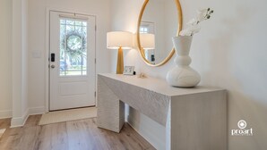 A modern entryway with a white door, a textured console table, a wall-mounted mirror, and a vase with white flowers. - Elegant Home 4BR/2BA Minutes From 30A & Sandestin Shopping (Santa Rosa Beach)