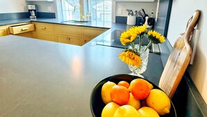 Una cocina con una isla grande, una cafetera y un bol con limones y girasoles en la encimera.