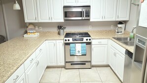 Una cocina moderna con armarios blancos, una estufa de acero inoxidable, un microondas y una cafetera.