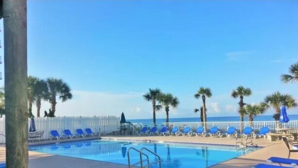 Zona de piscina con sillones reclinables azules, una piscina y vista al océano.
