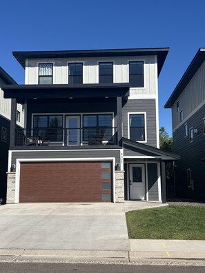 Une maison moderne à deux étages, dotée d’un garage, d’une porte d’entrée et d’un petit porche.