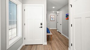 Un couloir avec une porte blanche, un banc et un tableau coloré accroché au mur.