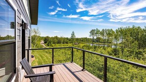 Une terrasse en bois, dotée d’une rambarde en métal, qui offre une vue imprenable sur un paysage verdoyant et luxuriant ainsi que sur un lac.