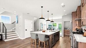 A modern kitchen with a central island, wooden cabinets, and pendant lighting.
