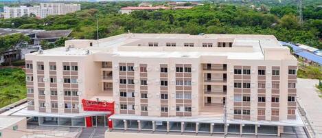 A multi-story hotel with a central atrium, a parking lot with several cars, and a surrounding green landscape.
