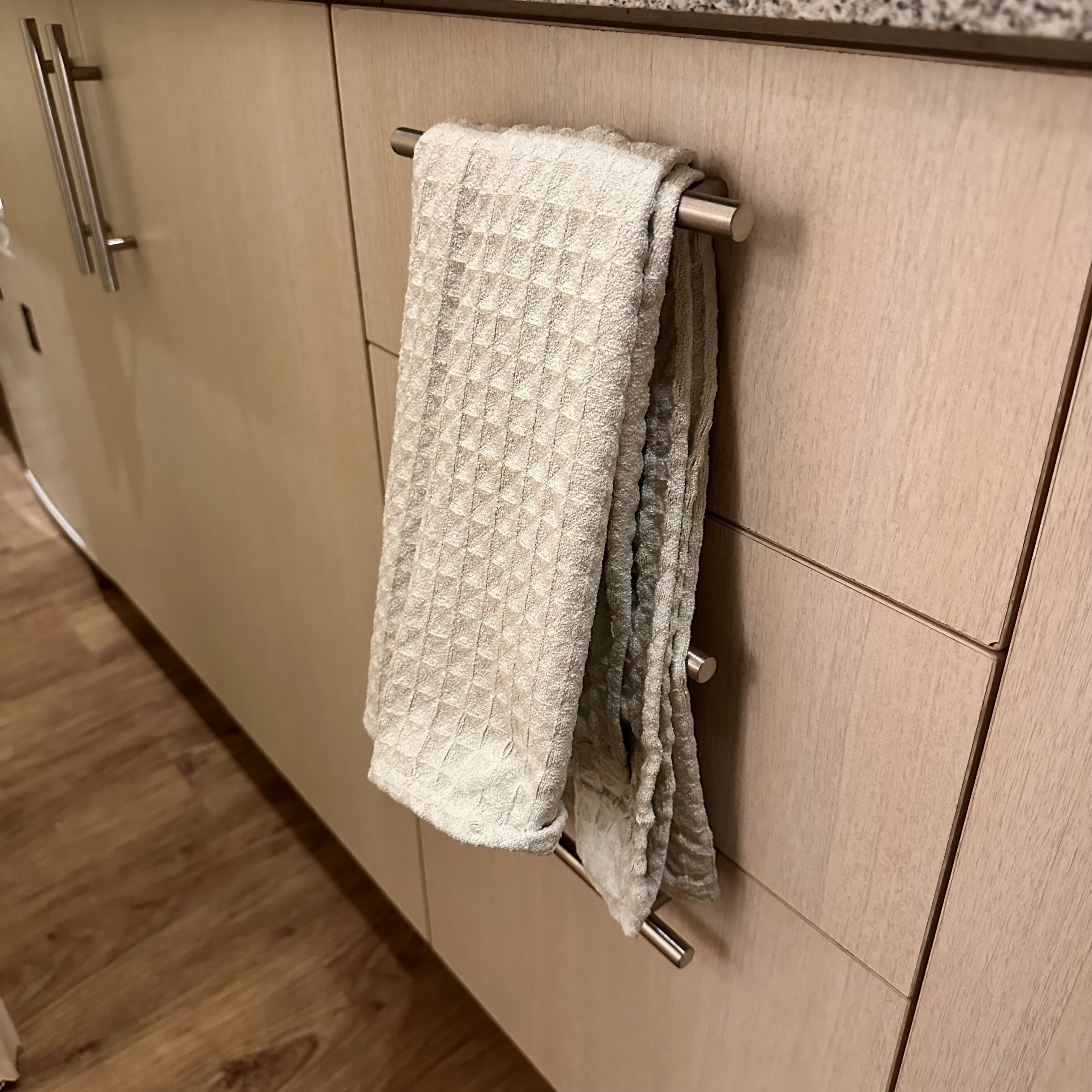 Une cuisine avec des meubles de rangement en bois et une serviette suspendue à une barre à serviettes en métal.