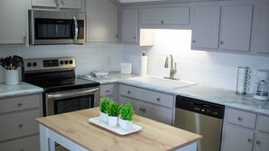 Una cocina moderna con armarios blancos, electrodomésticos de acero inoxidable, una mesa de madera y una encimera con fregadero y cafetera.
