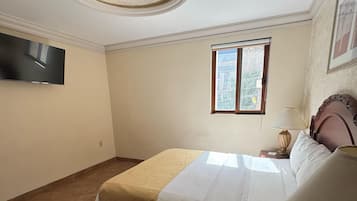A bedroom with a bed, a television, a window, and a lamp.