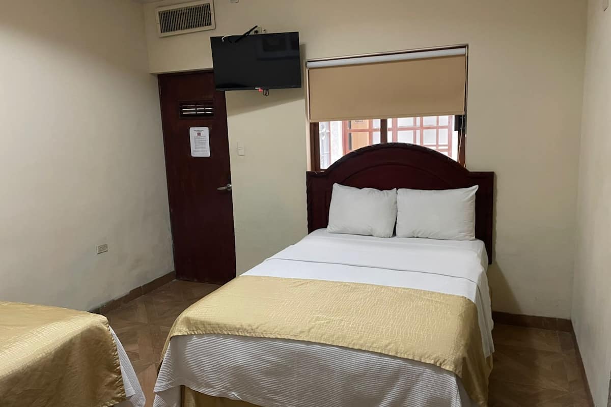 Um quarto pequeno e bem arrumado, com cama, guarda-roupa, televisão na parede e janela com persiana.