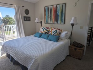 A bedroom with a large bed, two bedside lamps, a colorful abstract painting, and a view of the outdoors.