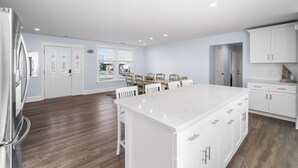 A modern kitchen with white cabinetry, a large island, and a dining area with wooden chairs.