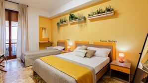 Een hotelkamer met twee bedden, een spiegel, een nachtkastje met een lamp en een wandplank met planten.