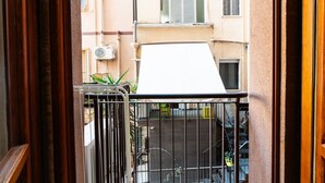 Een balkon met een metalen hekwerk, een witte luifel en uitzicht op een gebouw met ramen en een deur.
