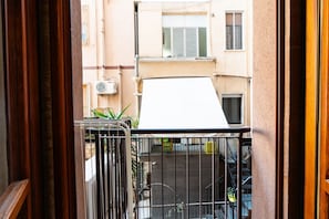 A balcony with a metal railing, a white awning, and a view of a building with windows and a door.