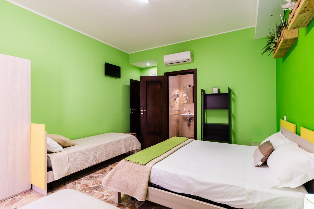 Habitació amb dos llits, un armari, un mirall, un lavabo i una estant amb plantes.