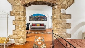 A room with a stone archway, a sofa, a patterned rug, and a painting on the wall. - GuestHost - The Arches of Ballarò - Cortile Scimeca Apartment (Palermo)