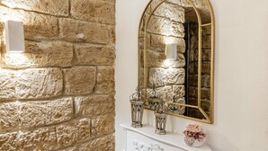 A stone wall, a white ornate fireplace, and a gold-framed mirror with candles. - GuestHost - The Arches of Ballarò - Cortile Scimeca Apartment (Palermo)