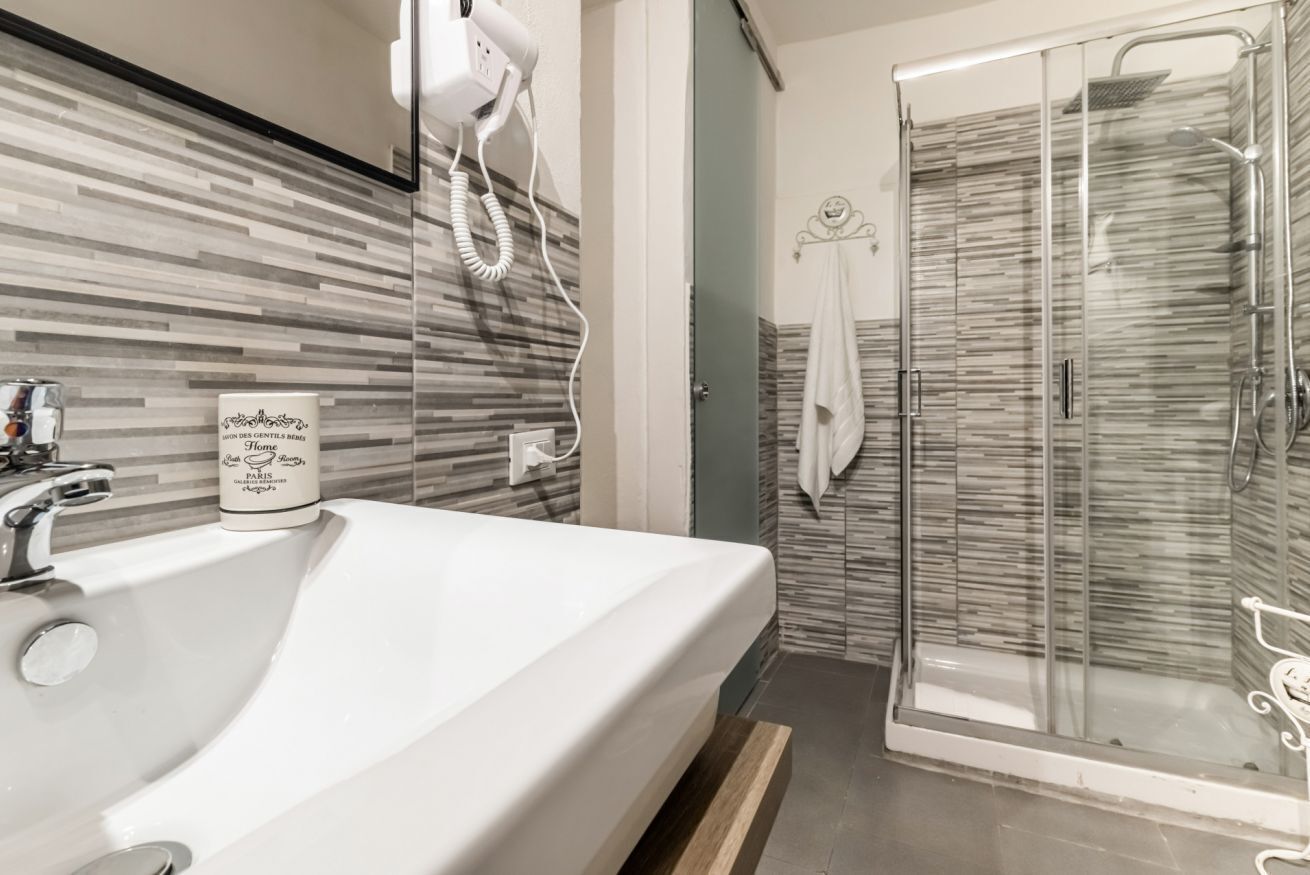 A bathroom with a large sink, a hairdryer, and a glass shower enclosure.